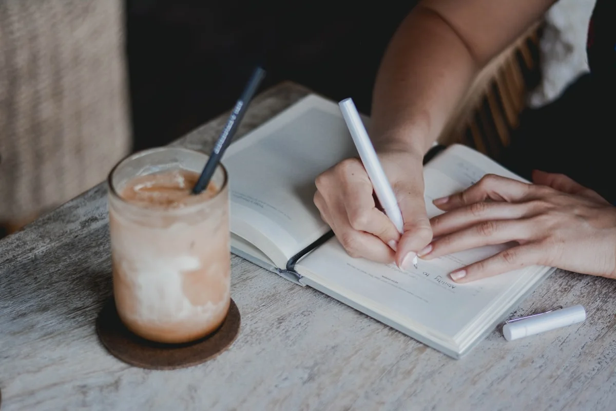best freelance jobs for writers without a degree - Woman writing in a journal and having coffee