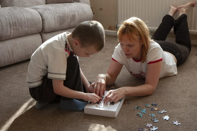 tips for remote learning with children at home US - Young boy assembling a colourful jigsaw puzzle on the carpet with his mother at home