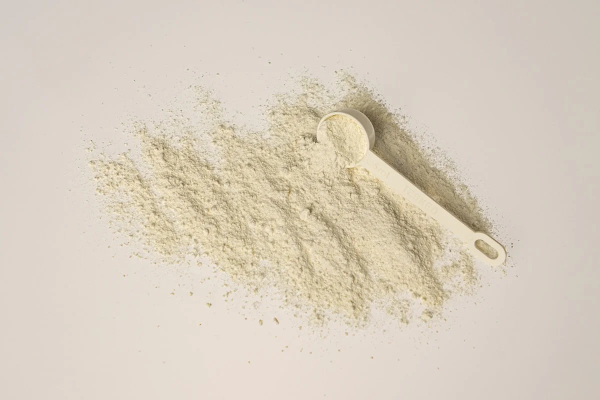 Close-up of a shaker bottle with perfectly mixed plant-based protein powder next to a clumpy, poorly mixed one, on a desk with a laptop and coffee.